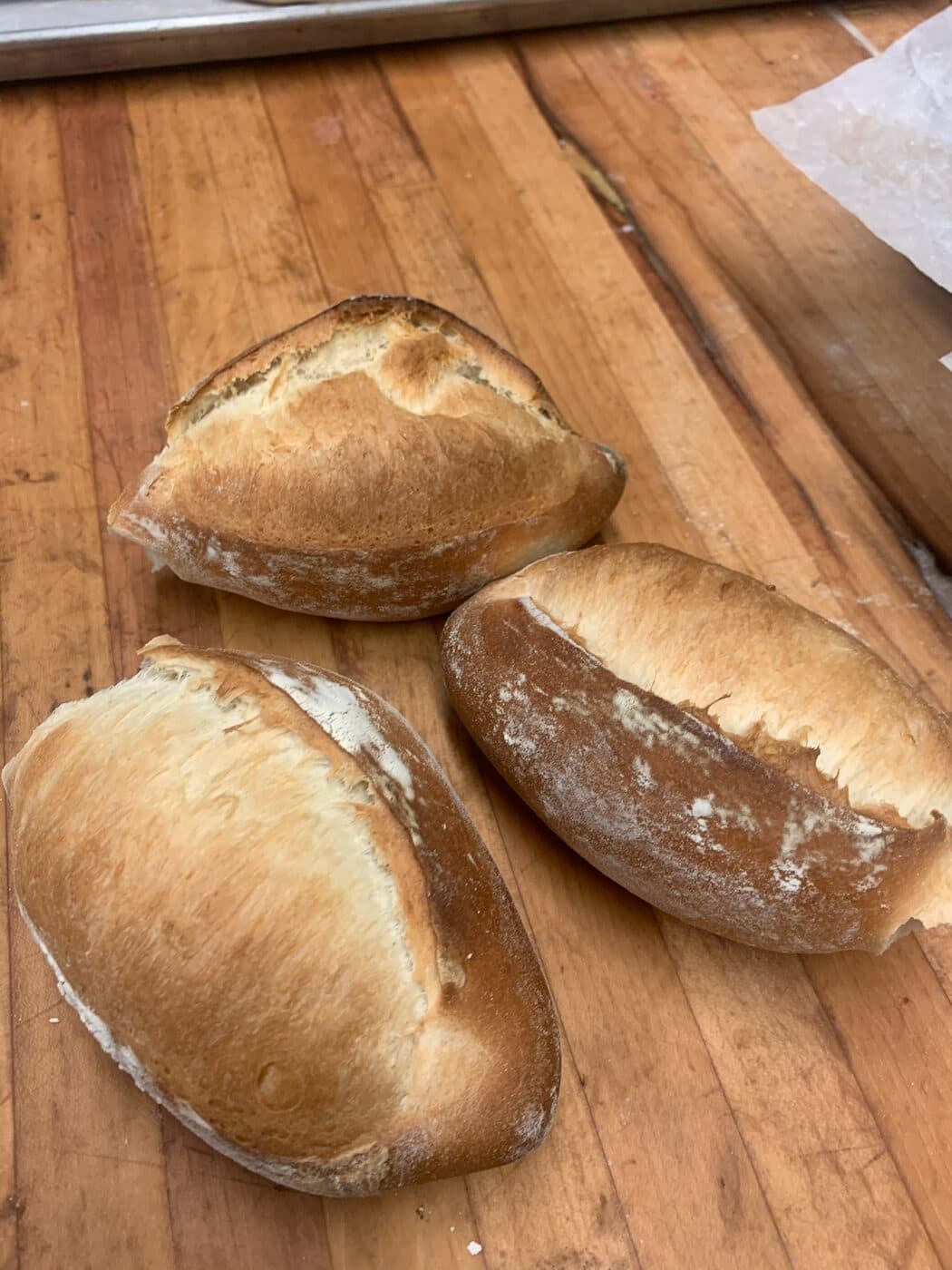 Three freshly baked bolillos with golden crusts on a wooden bakery table