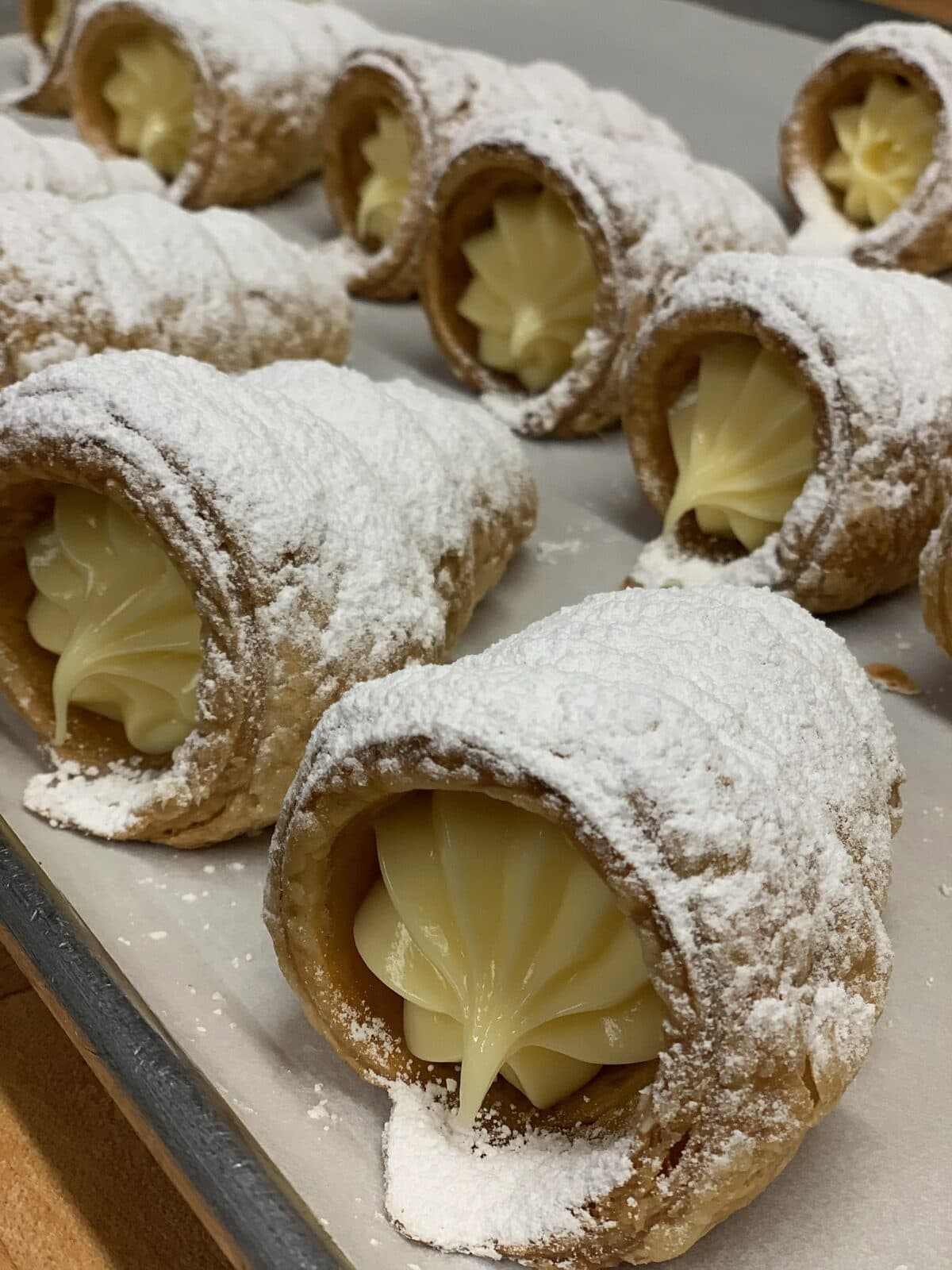 Rows of cream-filled cono pastries dusted with powdered sugar on a baking sheet
